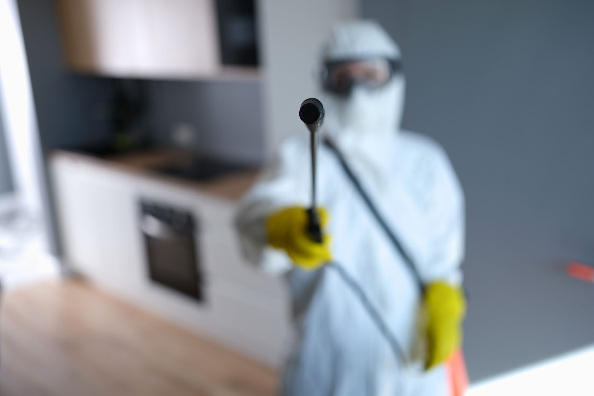 Disinfector in protective suit holding spray with liquid to kill insects closeup